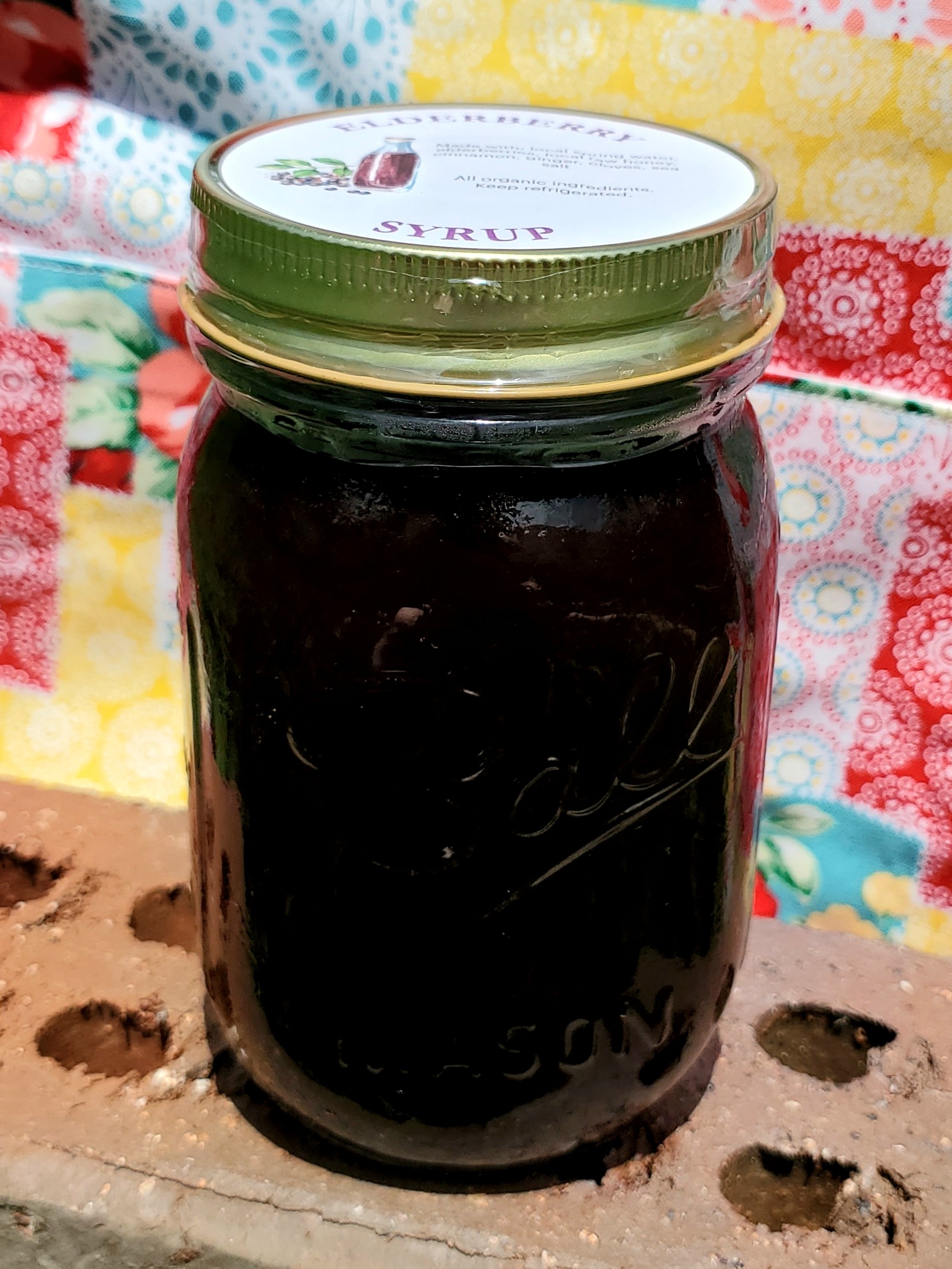 Jar of elderberry syrup on brick with quilt background